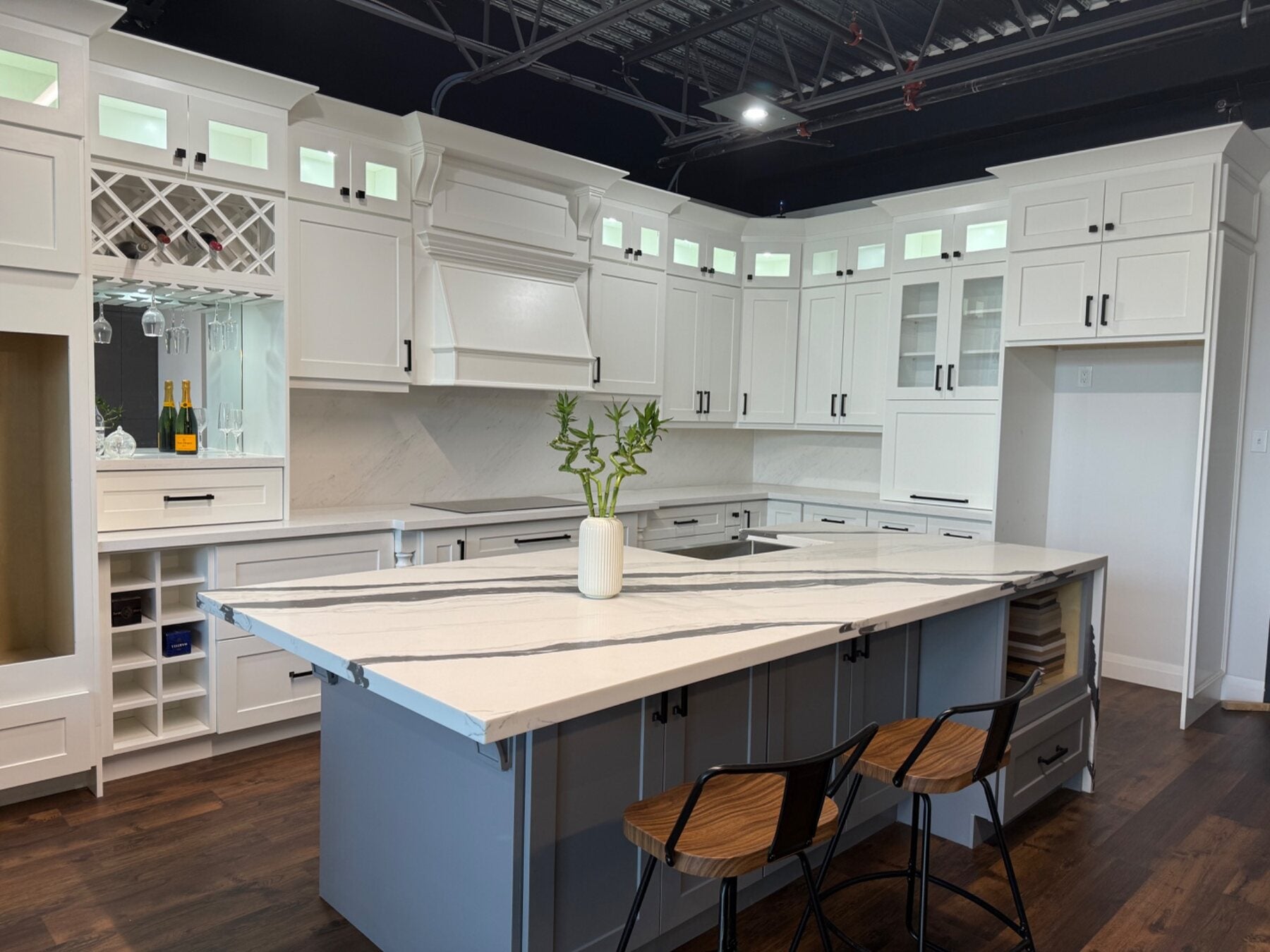 White showroom kitchen display with decorative hood, glass-front cabinets, wine storage and a large island
