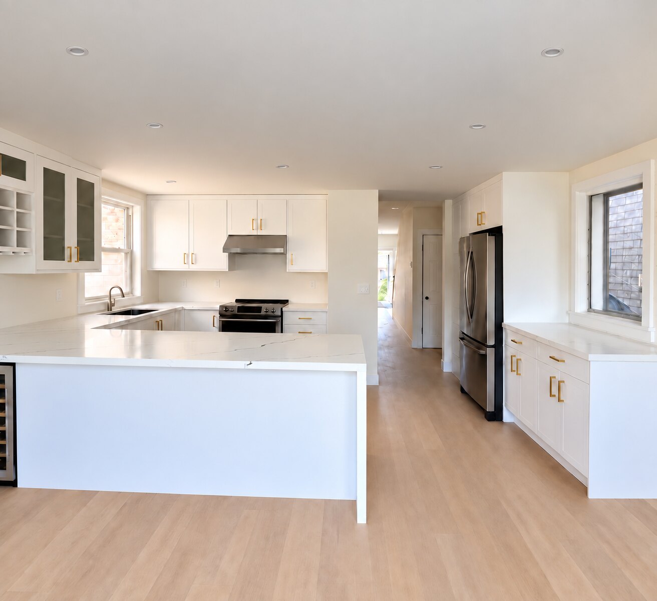 Completed white Shaker kitchen with glass-front display cabinets, wine storage, quartz countertops and brass hardware
