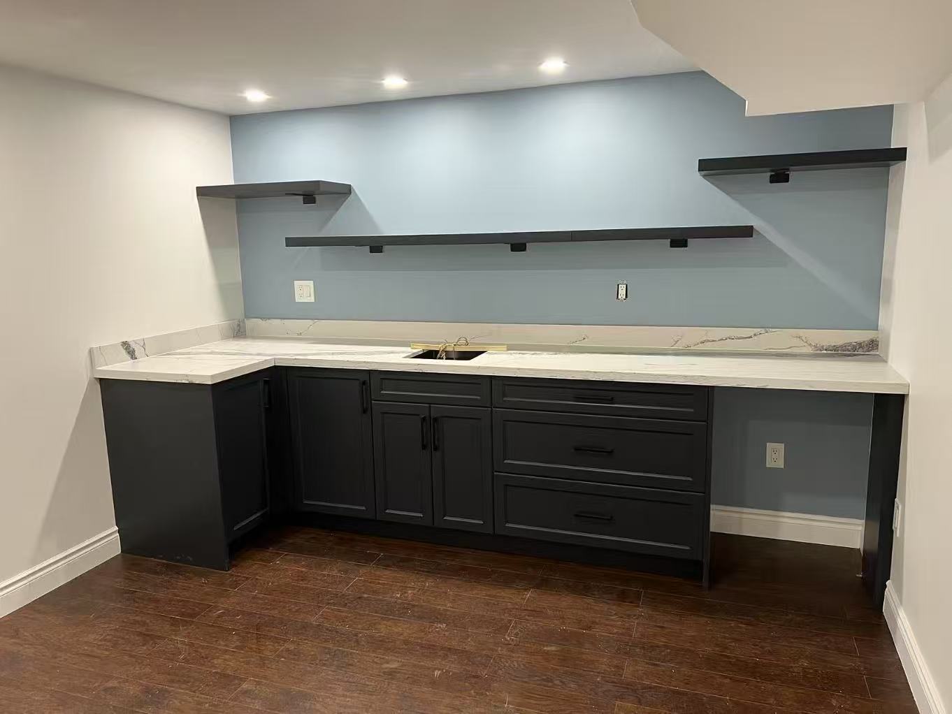 Compact basement kitchenette with dark Shaker cabinetry, countertop and open shelving
