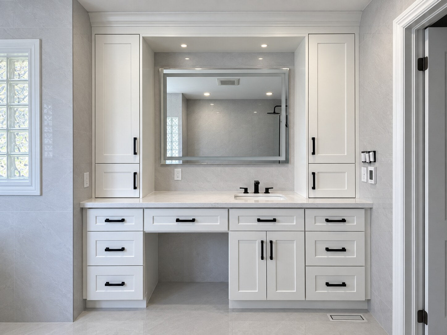 Large white built-in vanity with two storage towers, quartz countertop, makeup opening and black hardware